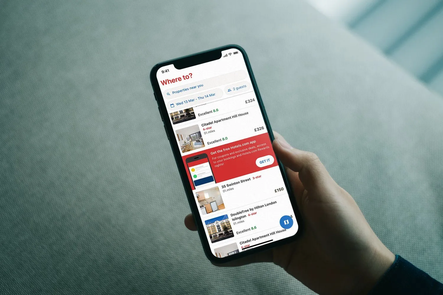 A hand holds a phone. The Hotels.com list is light, with Citadel Apartment Hill House, a red banner for the free app, and the DoubleTree by Hilton.