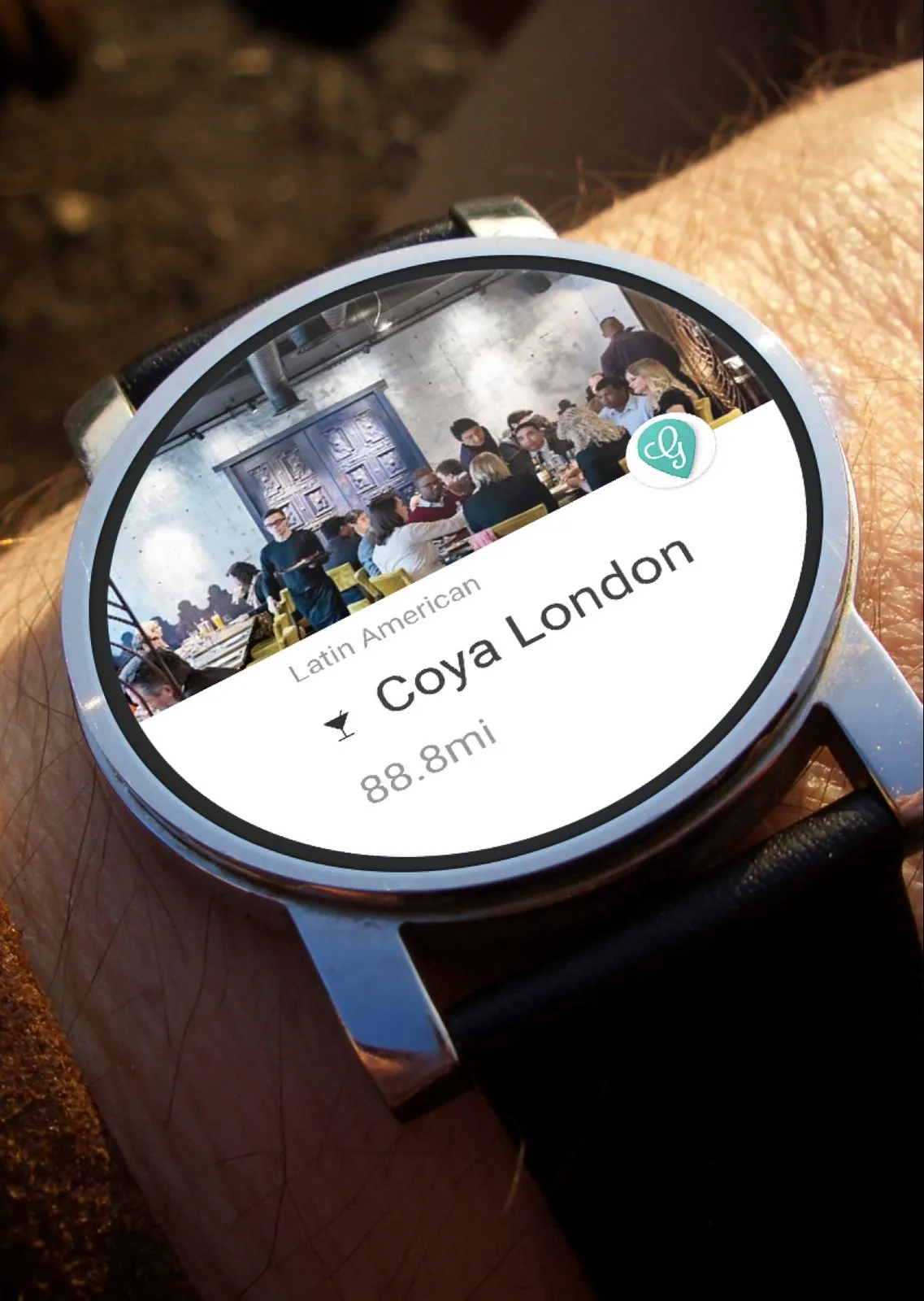 A round watch on a wrist. The screen is a Grabbd card for Coya London, Latin American, 88.8 miles away, with the teal pin.