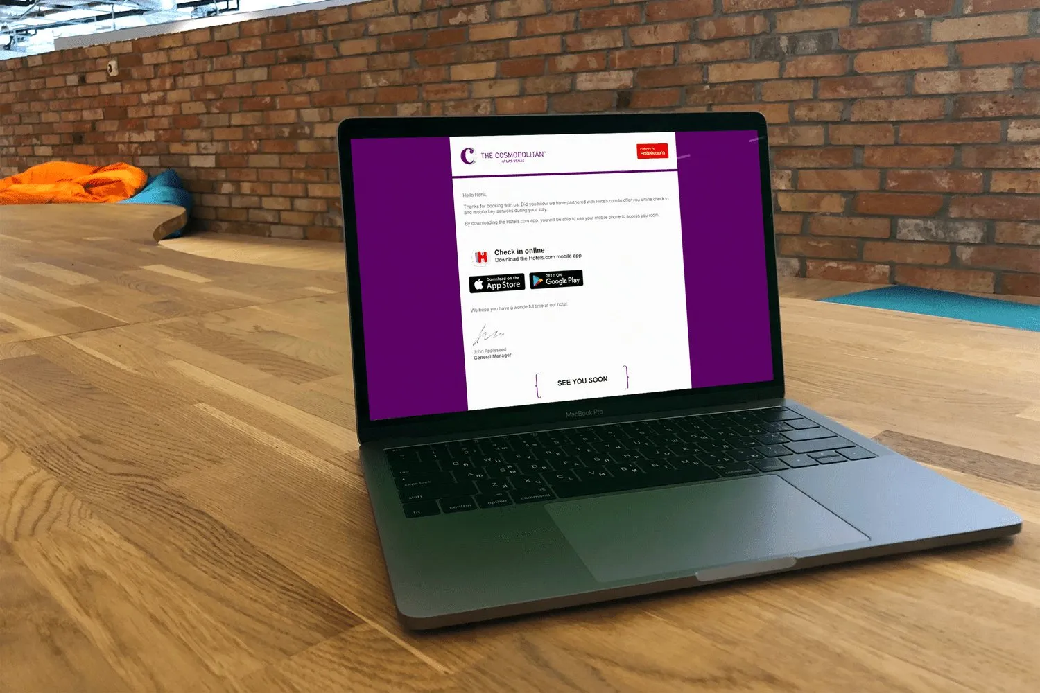 A laptop on a wooden reception desk. The screen is the Hotels.com mobile key, a purple page with a code.