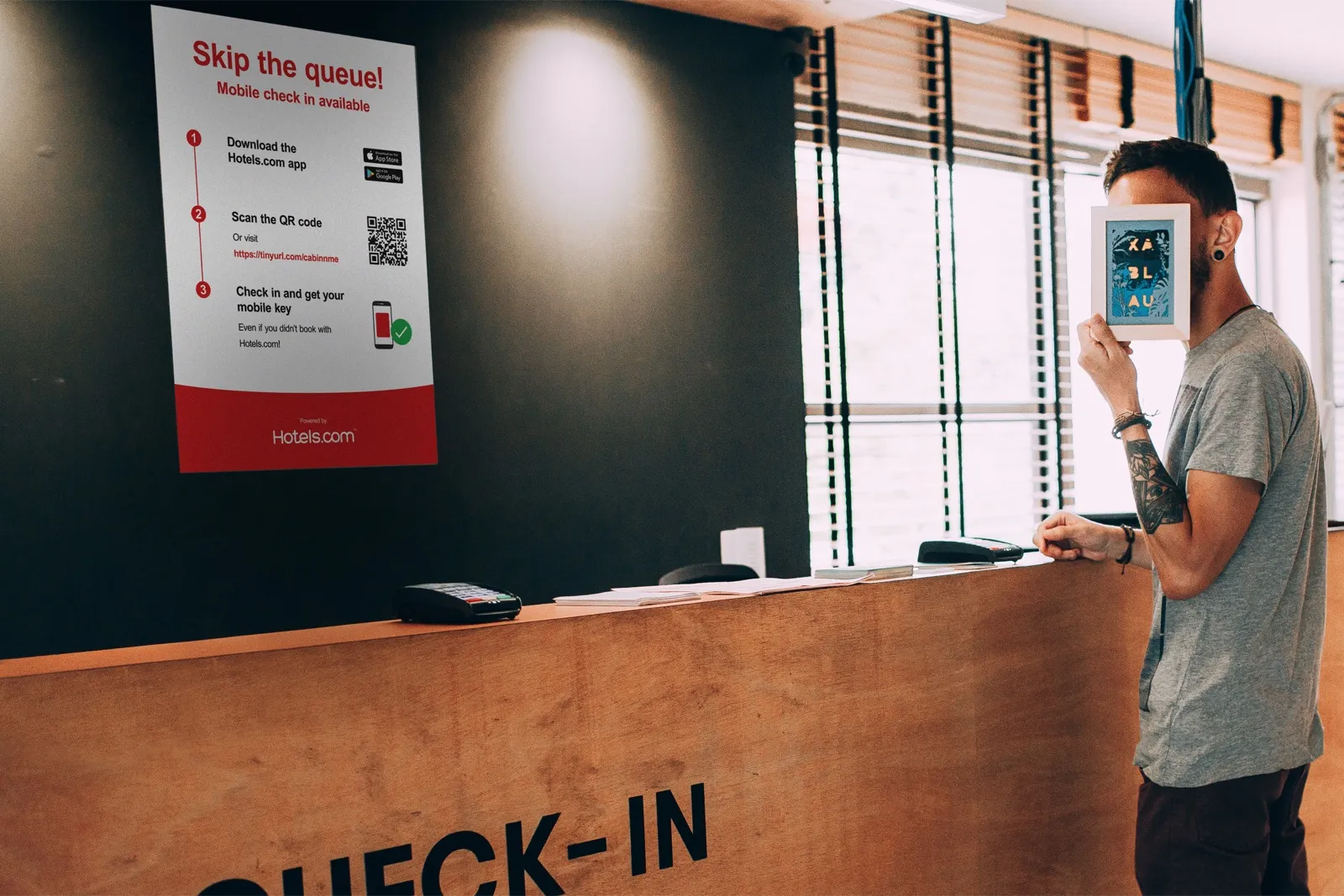 A hotel reception with a Hotels.com poster: skip the queue, download the app, scan a code, and check in for a mobile key.