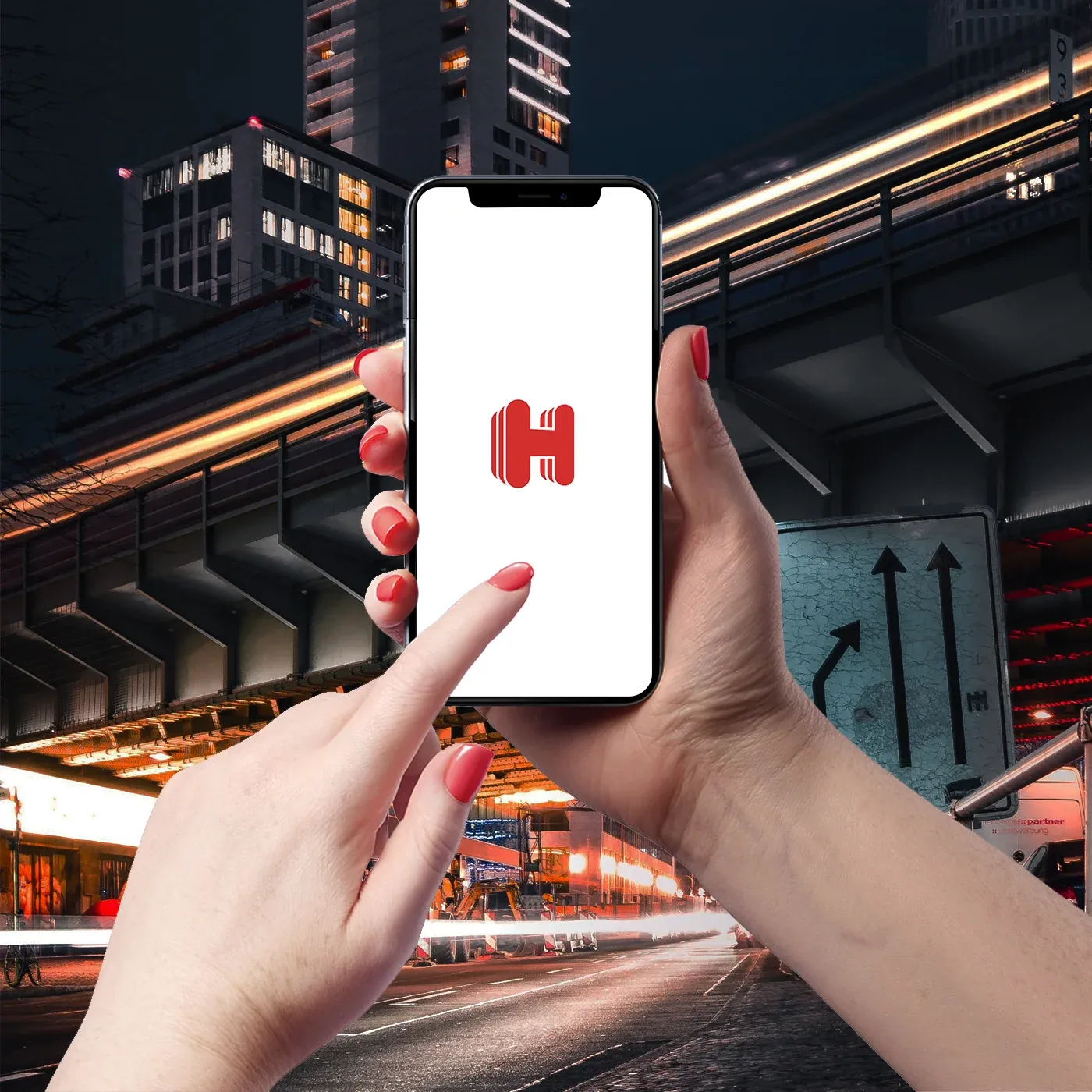 Hands holding a phone that shows a red Hotels.com H, against a night street and a one-way sign.
