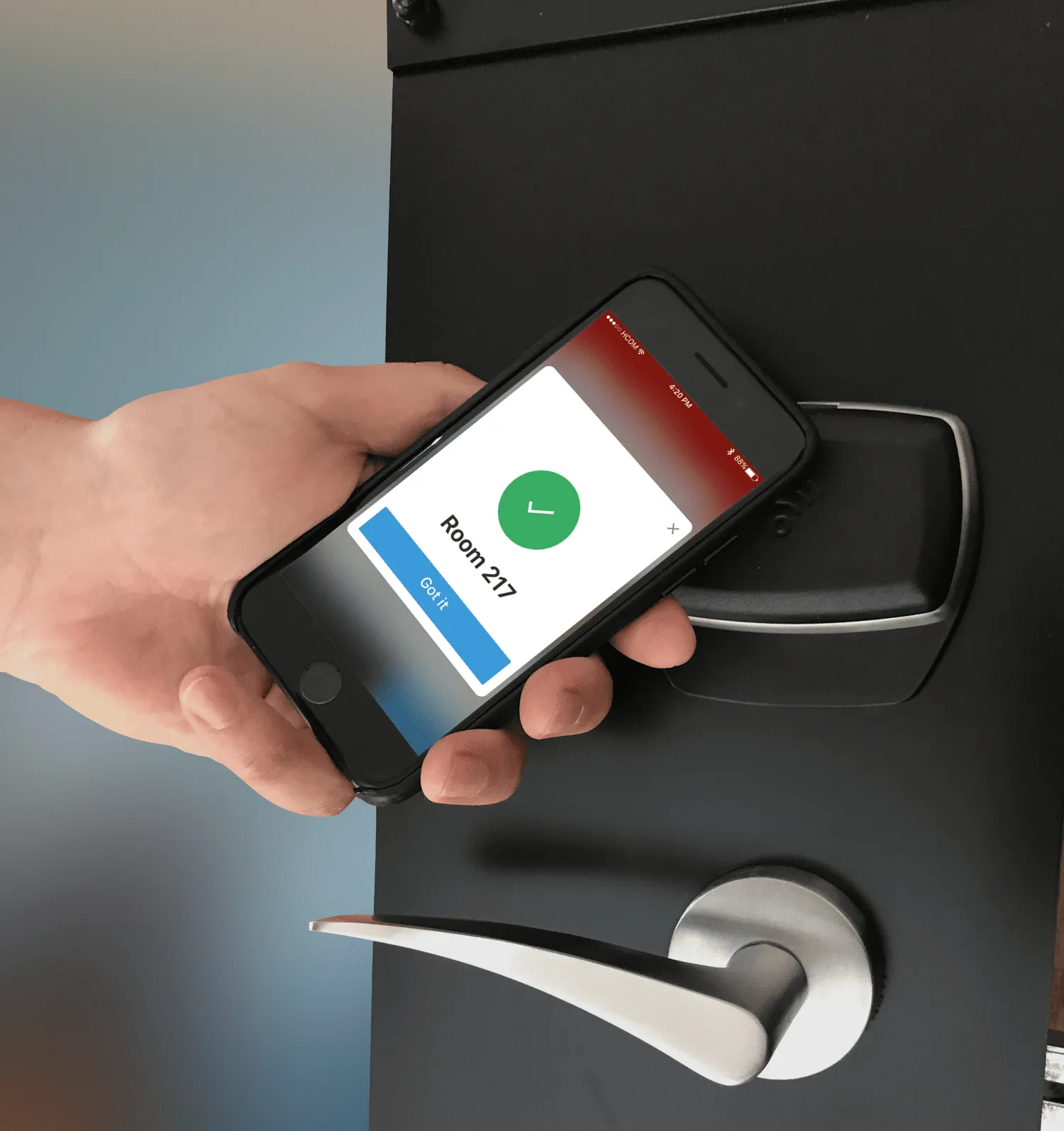 A hand holds a phone against a black hotel lock. The screen shows a green tick, Room 217, and a blue Got it button.
